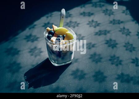Joghurt mit Früchten im Glas auf schwarzem Tisch mit Schatten Stockfoto