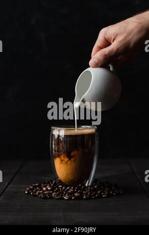 Hand Gießen Creme in Klarglas Tasse Kaffee auf schwarzem Hintergrund. Stockfoto