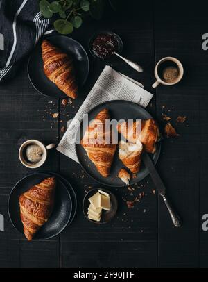 Teller mit Croissants mit Kaffee und Marmelade auf schwarzem Tisch von oben. Stockfoto