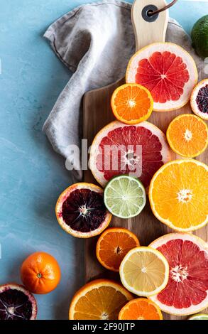 Scheiben von verschiedenen Zitrusfrüchten auf Schneidebrett auf blauem Hintergrund. Stockfoto
