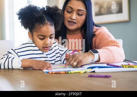 Großmutter lehrt niedliche Enkelin Färbung mit Buntstiften im Buch Stockfoto