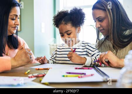 Mutter und Großmutter mit fröhlichem Mädchen zeichnen mit Buntstift auf Papier zu Hause Stockfoto