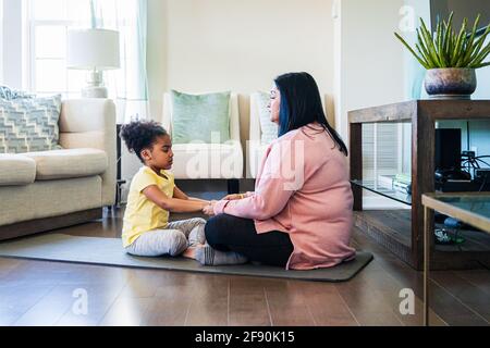 Großmutter praktiziert Meditation mit Enkelin, während sie auf einer Übungsmatte sitzt Im Wohnzimmer zu Hause Stockfoto