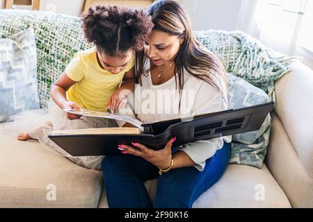 Mutter und Tochter schauen sich das Fotoalbum an, während sie sitzen Sofa zu Hause