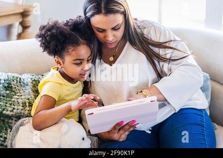 Mutter und Tochter verwenden ein digitales Tablet, während sie auf dem Sofa sitzen Zu Hause Stockfoto