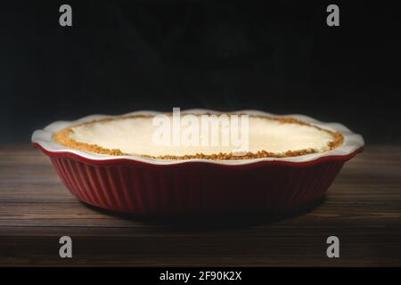 Käsekuchen in einer Auflaufform. Klassischer Käsekuchen im New Yorker Stil auf Holzhintergrund. Stockfoto