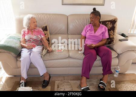 Die 93-jährige Frau spielt Karten mit ihrer Gesundheitshilfe zu Hause. Frau hat degenerative kognitive Beeinträchtigungen, die eine Aufsicht erfordern. Stockfoto
