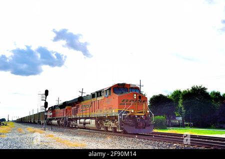 EARLVILLE, Illinois, USA. Ein Zug der Burlington Northern Santa Fe Railway in östlicher Richtung mit leeren Kohlewagen, die durch eine kleine Stadt in Illinois brüllen. Stockfoto
