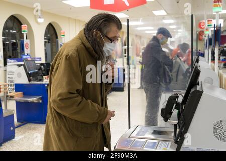 Ein Mann mit Brille, der eine Gesichtsbedeckung trägt, überprüft die Zahlungsoptionen beim Self-Service-Check-out in Tesco, London Stockfoto