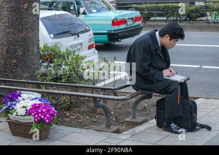 Japanischer Salaryman saß auf der Straße und arbeitete an einem Laptop, Omotesando, Tokio, Japan Stockfoto