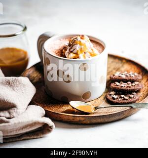Tasse heiße Schokolade, gekrönt mit Karamell beträufelt Schlagcreme, serviert auf einem Teller mit Schokoladenkeksen. Stockfoto
