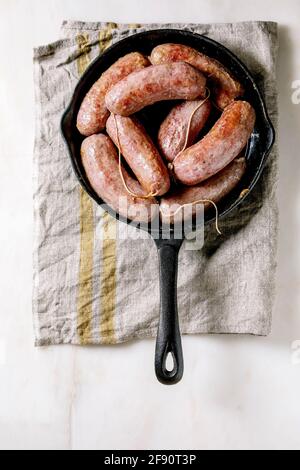 Gegrillte italienische Salsiccia-Würste in gusseiserner Pfanne auf Stoffservietten auf weißem Marmorboden. Flach liegend, Platz Stockfoto