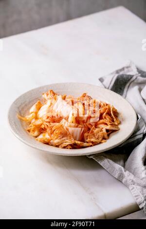 Hausgemachte koreanische traditionelle fermentierte Vorspeise Kimchi Kohl serviert in Keramikplatte über weißem Marmortisch. Stockfoto