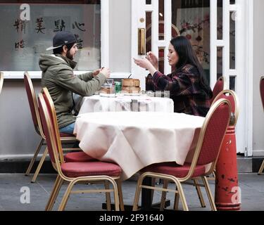 Zwei Gäste, die auf einem Gehsteig sitzen, genießen Dimsum in Londons Chinatown, während sich die Einschränkungen des Coronavirus lockern und die Gastfreundschaft im Freien in England zurückkehrt. Stockfoto