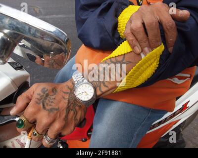 Ein Motorrad-Taxifahrer im Stadtzentrum von Bangkok zeigt seine Tattoos und andere Accessoires auf seiner Hand Stockfoto