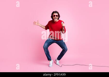 Foto-Portrait des tanzenden singenden Mannes, der das Mikrofon in der Hand hält Tragen von Sonnenbrillen isoliert auf pastellrosa Hintergrund Stockfoto