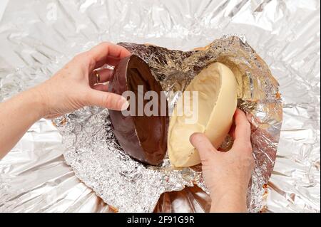 Osterei – Nahaufnahme der Hände beim Auspacken von Schokoladeneiern, die in Aluminiumfolie eingewickelt sind. Draufsicht. Stockfoto