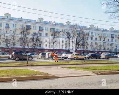Moskau. Russland. 06. April 2021. Orangefarbene uniformierte Hausmeister, die auf einer Straße in der Stadt den Rasen fegen. Sonniger Frühlingstag. Die Arbeit der Gemeinde Stockfoto
