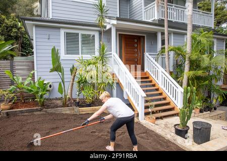 Australische Frau Modell freigegeben arbeiten auf dem Garten zu Hause Raking Boden, um für neue Rasen zu legen vorzubereiten, Sydney, NSW, Australien Stockfoto