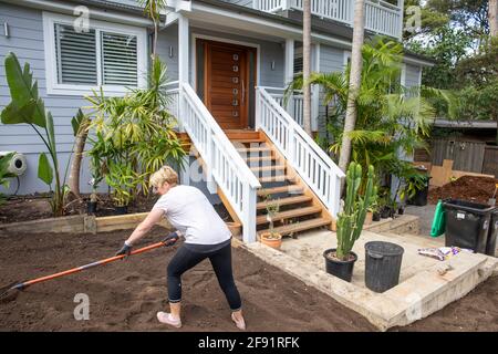 Australische Frau Modell freigegeben arbeiten auf dem Garten zu Hause Raking Boden, um für neue Rasen zu legen vorzubereiten, Sydney, NSW, Australien Stockfoto