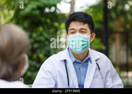 Asiatische Arzt im Gespräch mit älteren weiblichen Patienten auf Rollstuhl Stockfoto