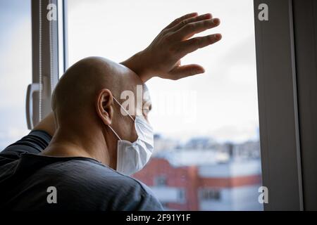 Porträt eines kahlen Mannes in einer Schutzmaske suchen Durch die Fenster zur Nahaufnahme der Straße Stockfoto