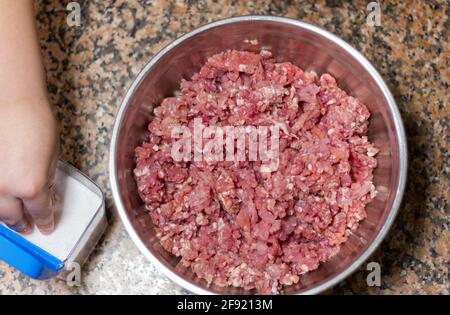 Der Schuss eines Kochs, der dem Hackfleisch Salz hinzufügt In einer Schüssel Stockfoto