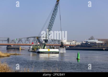 ZUTPHEN, NIEDERLANDE - 24. März 2021: Klaue eines Baggerschiffs, das aus dem Wasser steigt und Sedimente vor einer Zugbrücke entfernt, die den Wasserweg freimacht Stockfoto