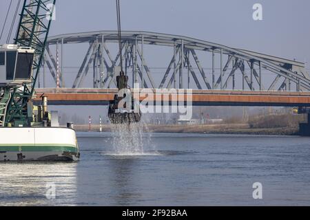 ZUTPHEN, NIEDERLANDE - 24. März 2021: Klaue eines Baggerschiffs, das aus dem Wasser steigt und Sedimente vor einer Zugbrücke entfernt, die den Wasserweg freimacht Stockfoto