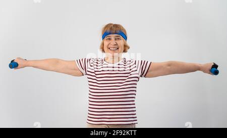 Glückliche alte Frau macht Fitnessübungen mit Hanteln auf weißem Hintergrund. Ältere Dame, die Fitness tut, um die Gesundheit zu erhalten. Stockfoto