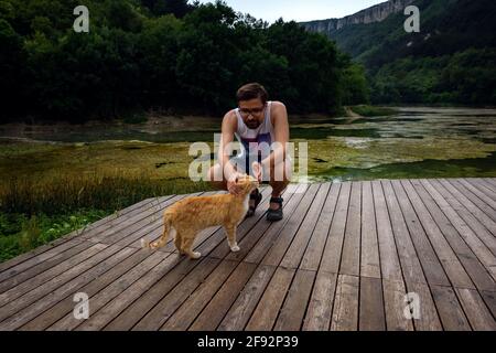 Ein Mann spielt mit einer heimische rot gestromte Katze. Die Katze reibt sich am mans Bein. Nach dem Regen Stockfoto