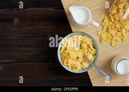 Draufsicht auf Cornflakes auf einem Teller und Milch auf einem Holzhintergrund. Platz für Text. Stockfoto