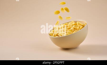Traditionelles Frühstück mit Cornflakes. Cornflakes fallen auf hellbeigem Hintergrund in eine Schüssel. Stockfoto