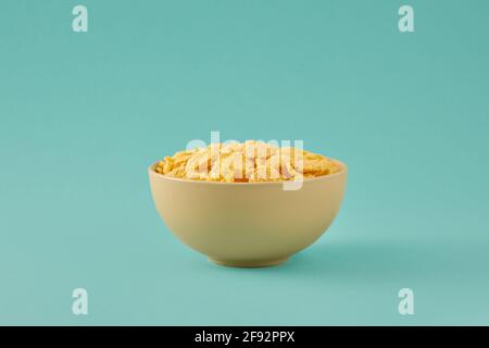 Traditionelles Frühstück mit Cornflakes. Cornflakes in einer hellbeigen Schale auf einem türkisfarbenen Hintergrund. Stockfoto