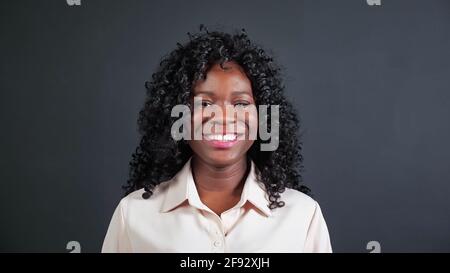 Attraktive junge afroamerikanische Frau mit lockigem Haar lächelt und lacht Blick in die Kamera auf schwarzem Hintergrund in der Studioansicht Stockfoto