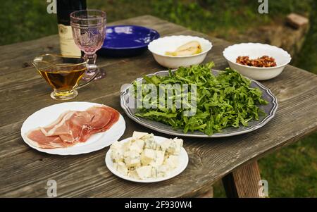 Zutaten für Rucola-Salat, Blauschimmelkäse, Prosciutto, Birne und karamellisierte Nüsse auf einem alten Tisch Stockfoto