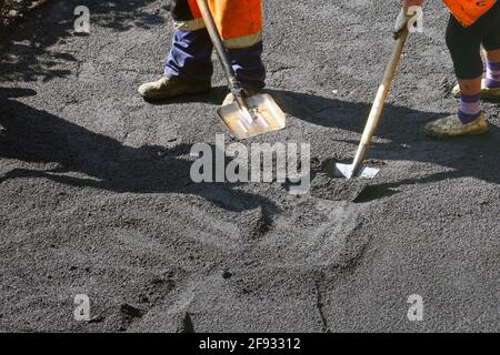 Straßenreparaturarbeiten. Arbeiter gleichen den Asphalt mit Schaufeln. Bauarbeiter während der Asphaltstraße. Handarbeit im Bauwesen Stockfoto