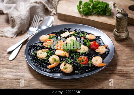 Teller mit schwarzer Pasta mit Garnelen und Gemüse auf einem Holztisch Stockfoto