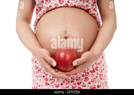Eine Schwangerin hält einen großen roten Apfel in der Nähe ihres großen Bauch Stockfoto