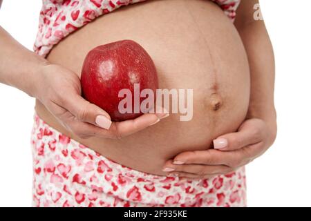 Eine Schwangerin hält einen großen roten Apfel in der Nähe ihres großen Bauch Stockfoto