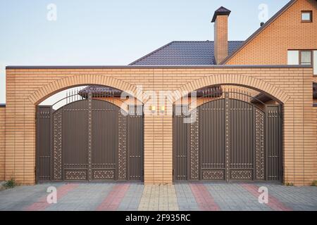 Hoher Ziegelzaun und zwei Metalltore Stockfoto