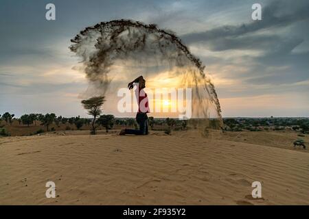 Nicht identifizierter Mann wirft mit Sand in der Luft in der Wüste jaisalmer, rajasthan. Stockfoto