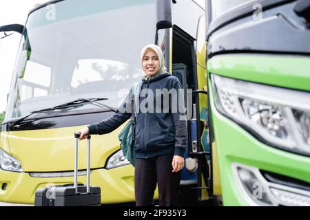 Eine Frau in einem Schleier lächelt und schaut auf die Kamera Während Sie einen Koffer halten Stockfoto