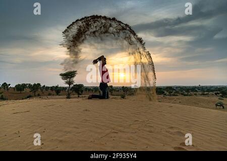 Nicht identifizierter Mann wirft mit Sand in der Luft in der Wüste jaisalmer, rajasthan. Stockfoto