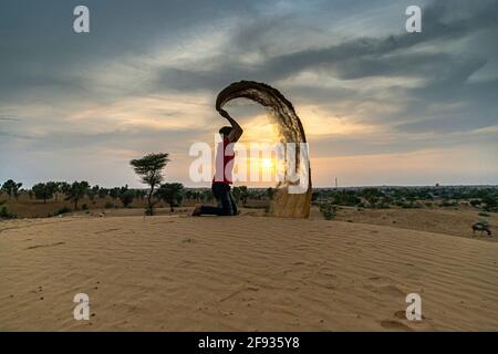 Nicht identifizierter Mann wirft mit Sand in der Luft in der Wüste jaisalmer, rajasthan. Stockfoto