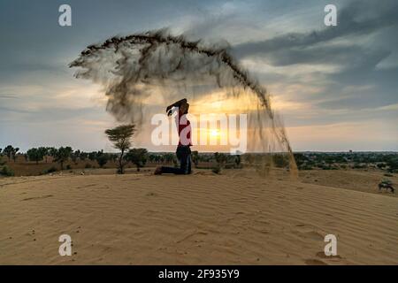 Nicht identifizierter Mann wirft mit Sand in der Luft in der Wüste jaisalmer, rajasthan. Stockfoto