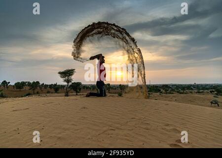 Nicht identifizierter Mann wirft mit Sand in der Luft in der Wüste jaisalmer, rajasthan. Stockfoto