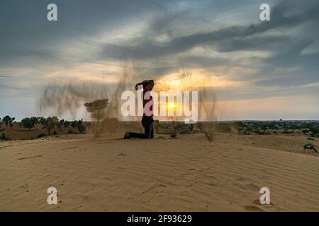 Nicht identifizierter Mann wirft mit Sand in der Luft in der Wüste jaisalmer, rajasthan. Stockfoto