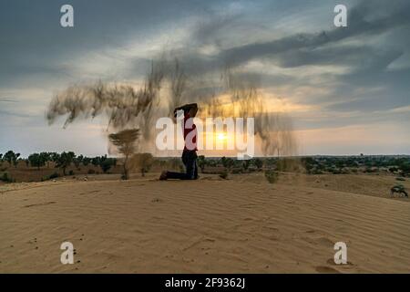 Nicht identifizierter Mann wirft mit Sand in der Luft in der Wüste jaisalmer, rajasthan. Stockfoto