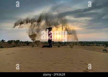 Nicht identifizierter Mann wirft mit Sand in der Luft in der Wüste jaisalmer, rajasthan. Stockfoto